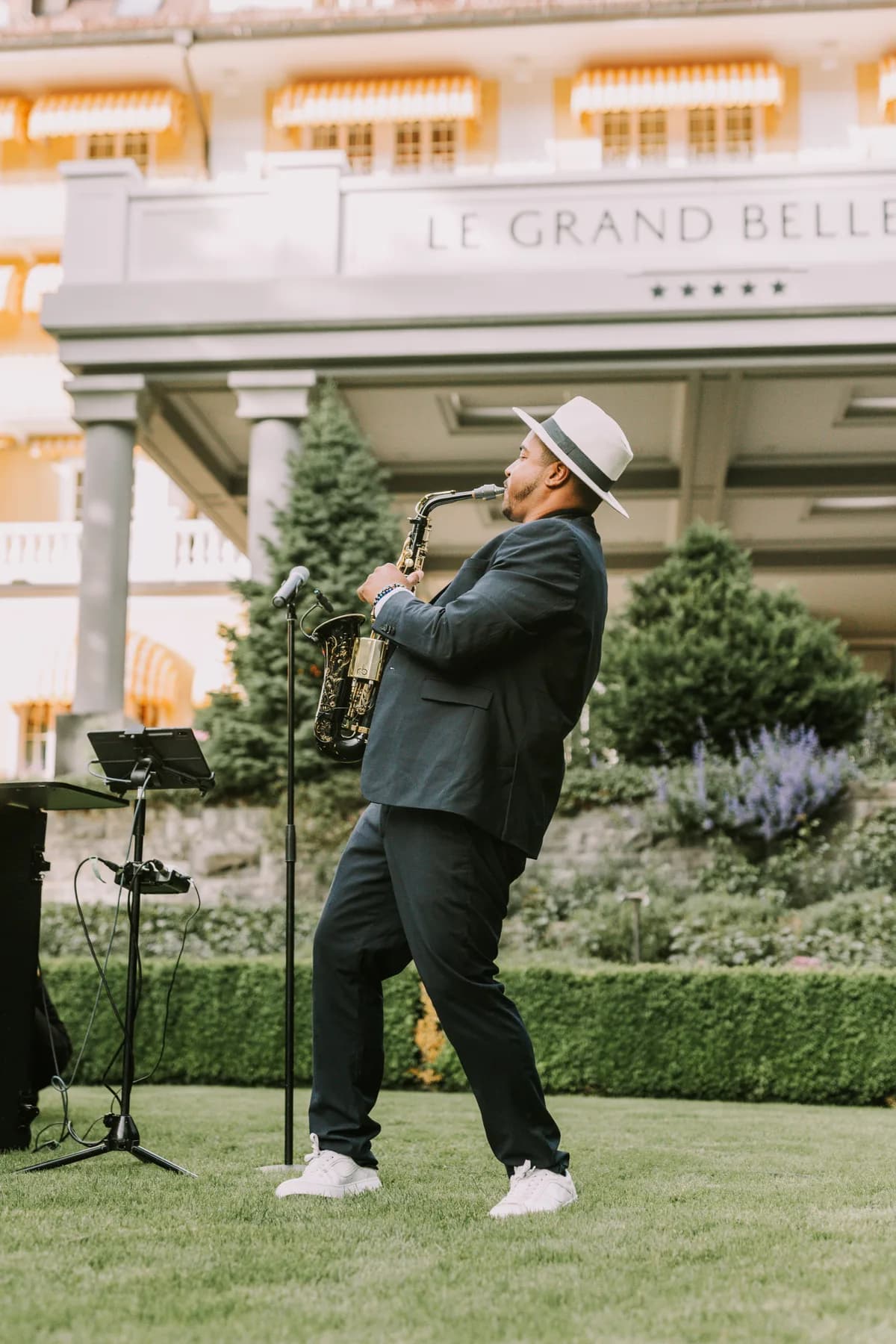 Ismaël K jouant du saxophone alto, panama blanc, devant un palace de Gstaad