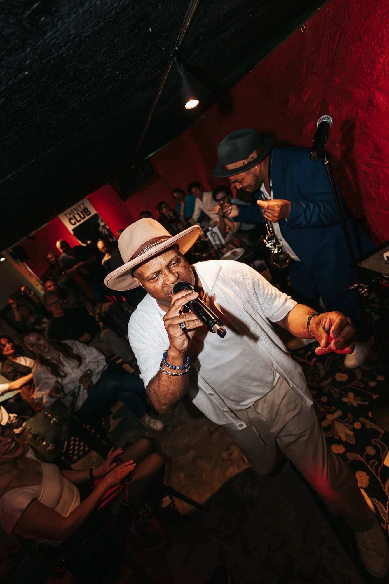 Chanteur au micro et saxophoniste au milieu du public d'un club