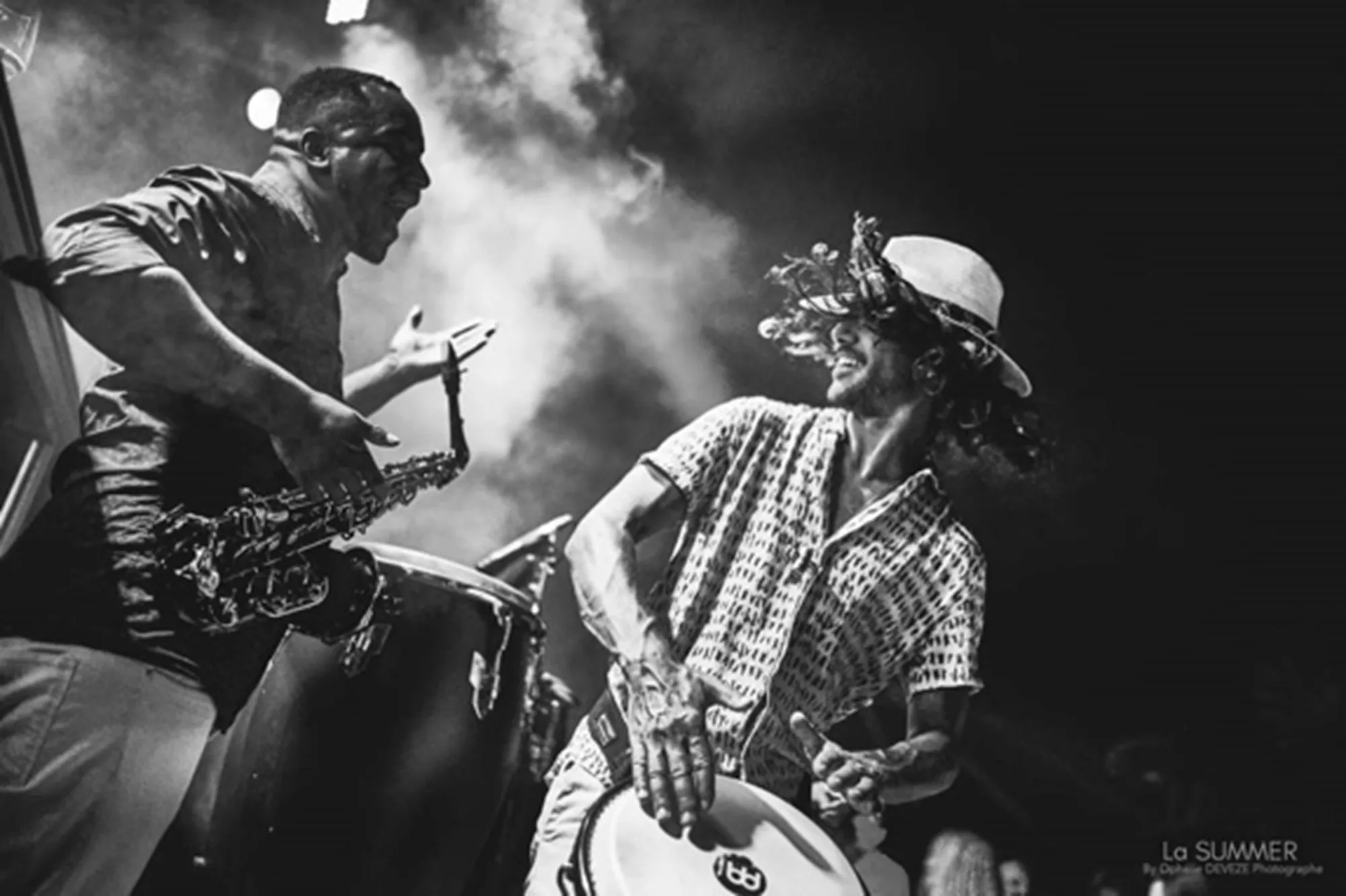Saxophonist and percussionist backlit in the smoke of a stage