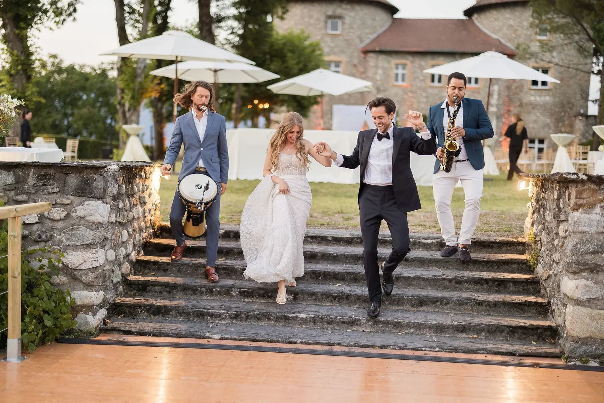Newlyweds making their entrance down a château staircase, accompanied by saxophone and percussion